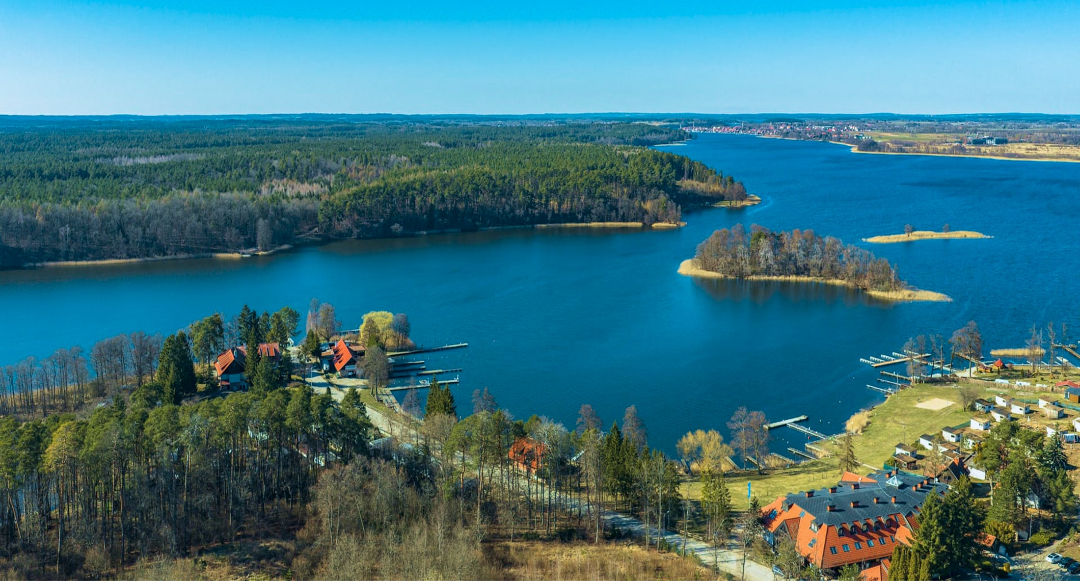 Panoramiczny widok jeziora z leśnymi wyspami, przystaniami i zabudowaniami nad brzegiem
