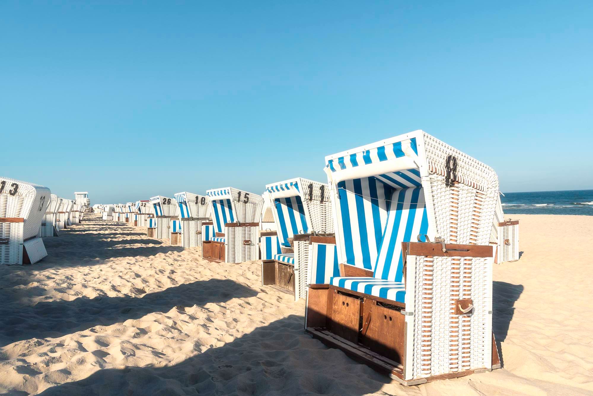 Rząd biało-niebieskich koszy plażowych na piaszczystej plaży nad morzem