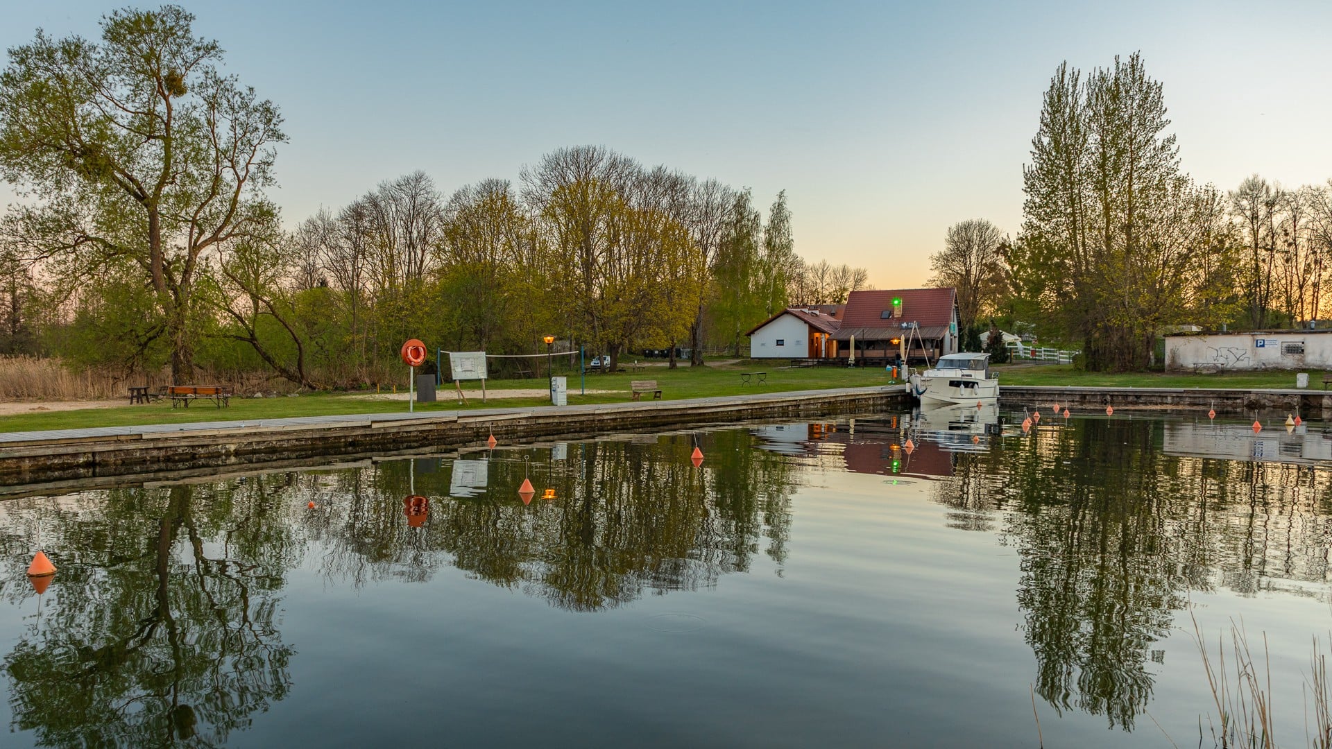 Śluza z łodzią, domem i pomostem nad spokojną wodą, otoczona drzewami o zmierzchu