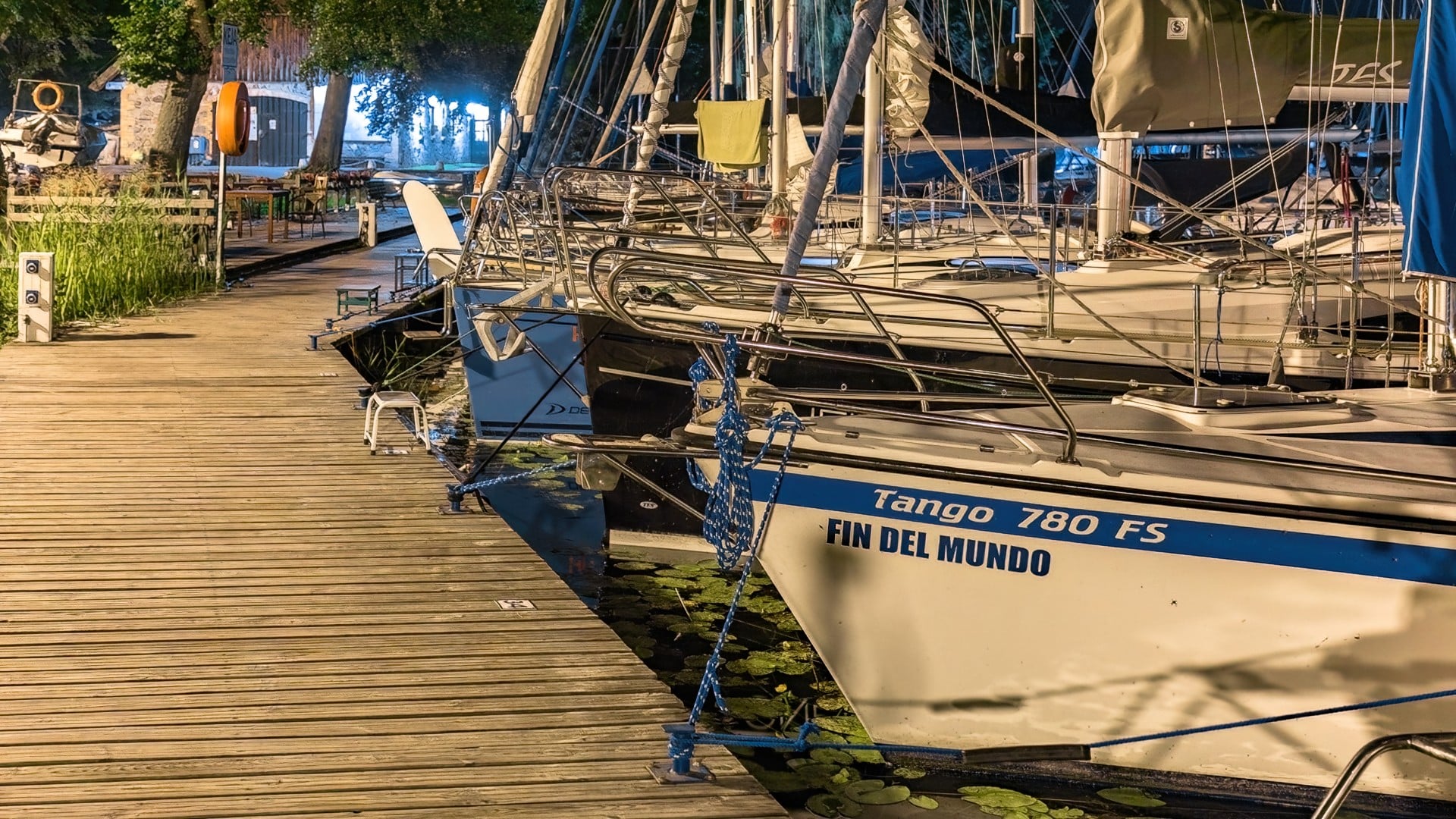 Łodzie żaglowe zacumowane przy drewnianym pomoście, z napisem „Tango 780 FS Fin del Mundo”