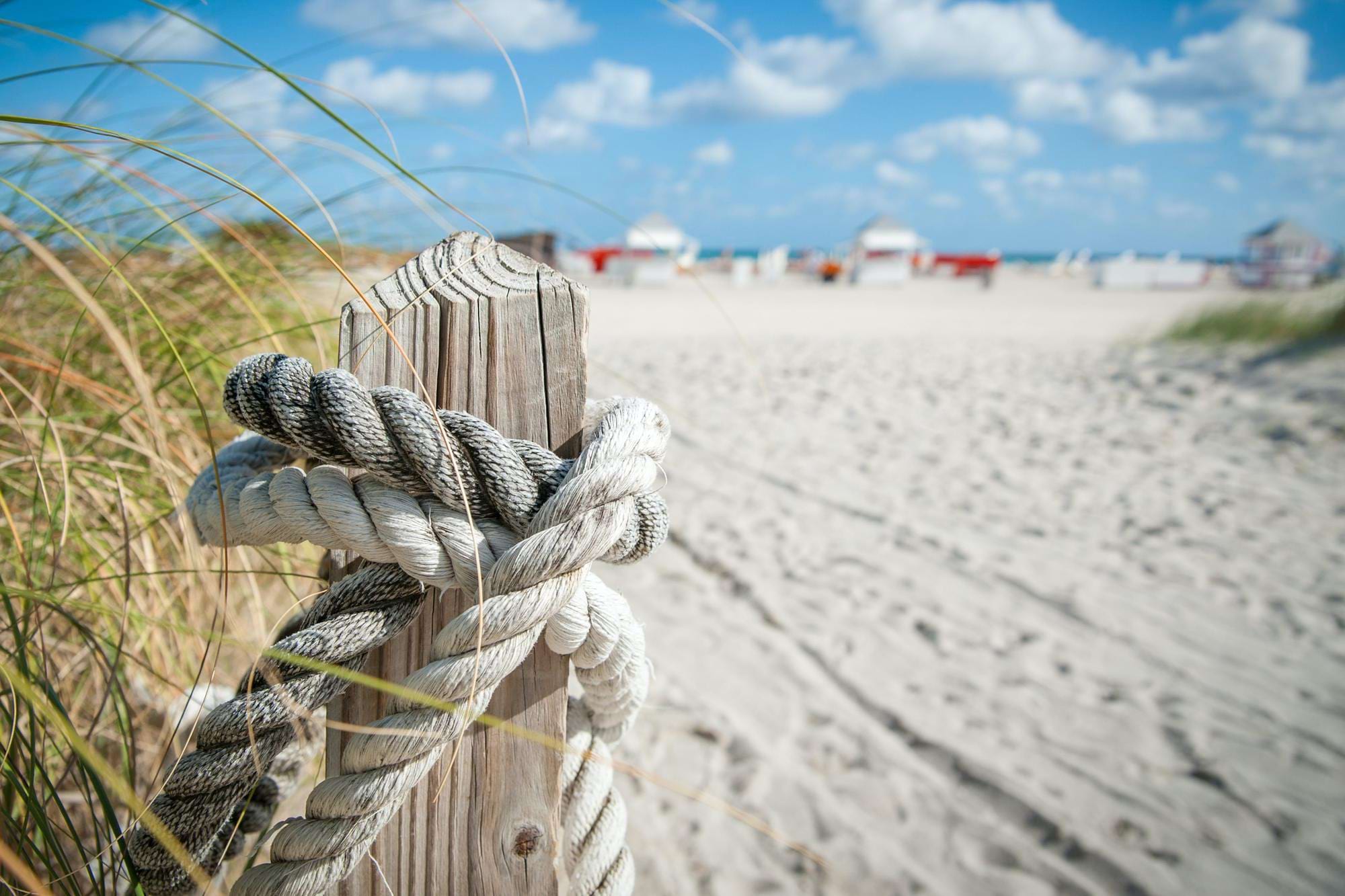 Drewniany słupek z grubą liną na wydmach, w tle piaszczysta plaża, morze i błękitne niebo