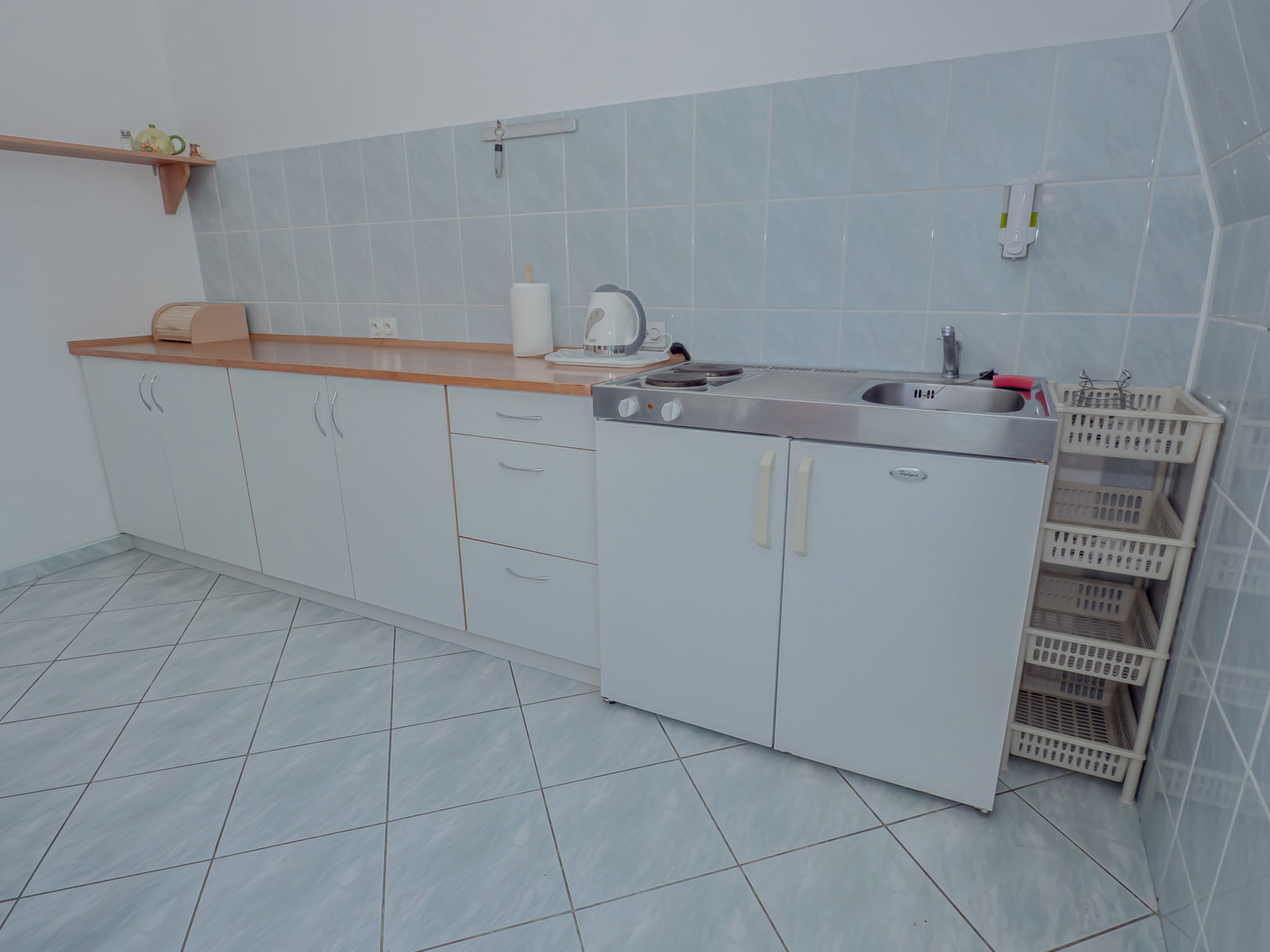 Jasna kuchnia z białymi szafkami, kuchenką, zlewem, czajnikiem i koszami na pranie