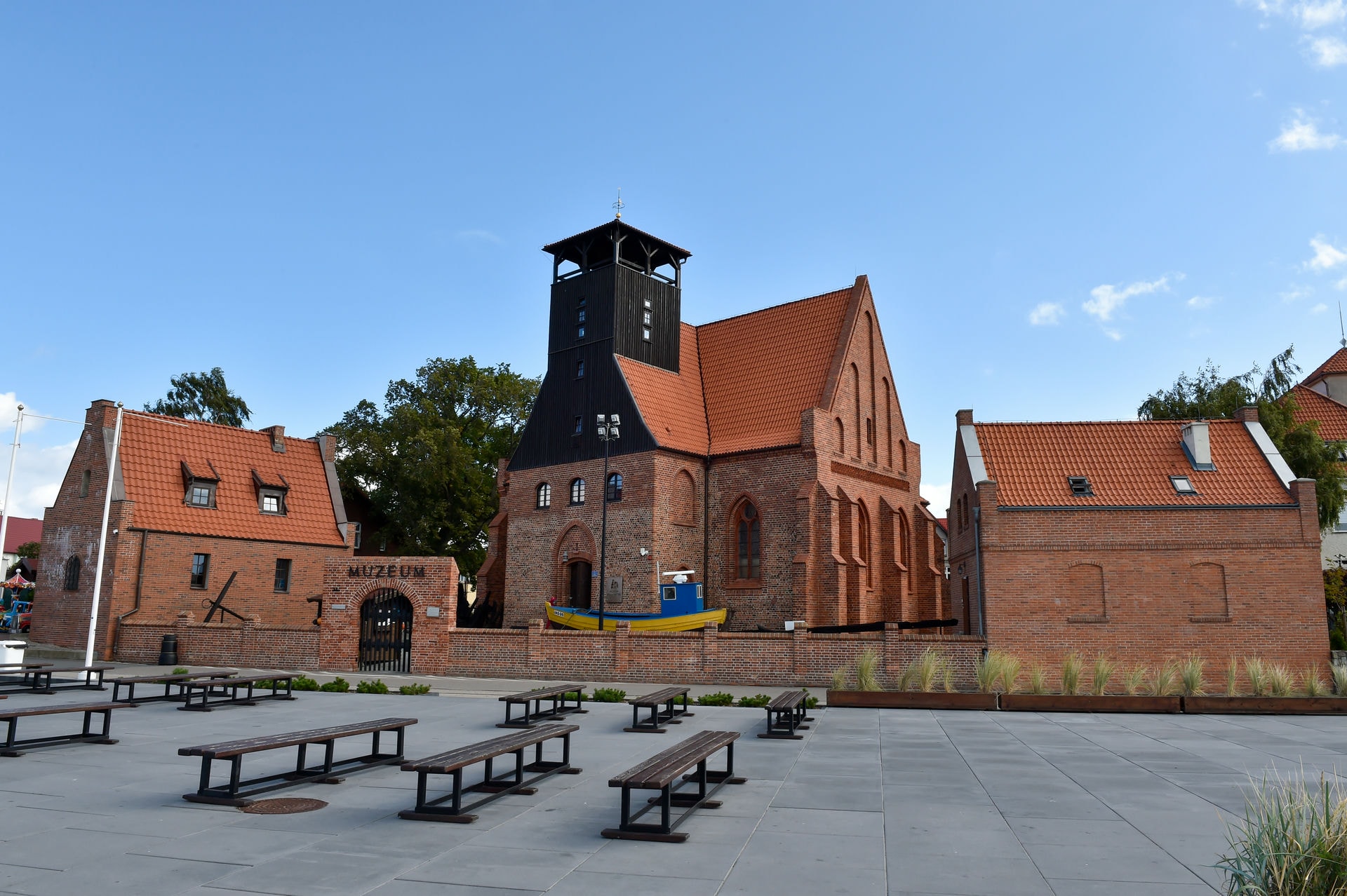 Ceglany budynek muzeum z wieżą, czerwonymi dachami i łodzią przed wejściem