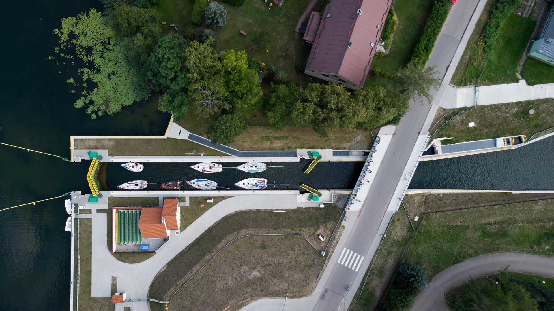 Widok z lotu ptaka na śluzę z zacumowanymi żaglówkami, jeziorem, drogą i otaczającą zielenią