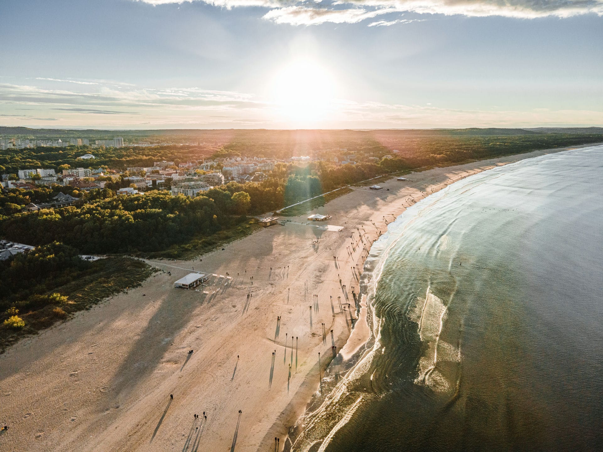 Lotniczy widok szerokiej piaszczystej plaży, morza, nadmorskiego miasta i zachodzącego słońca