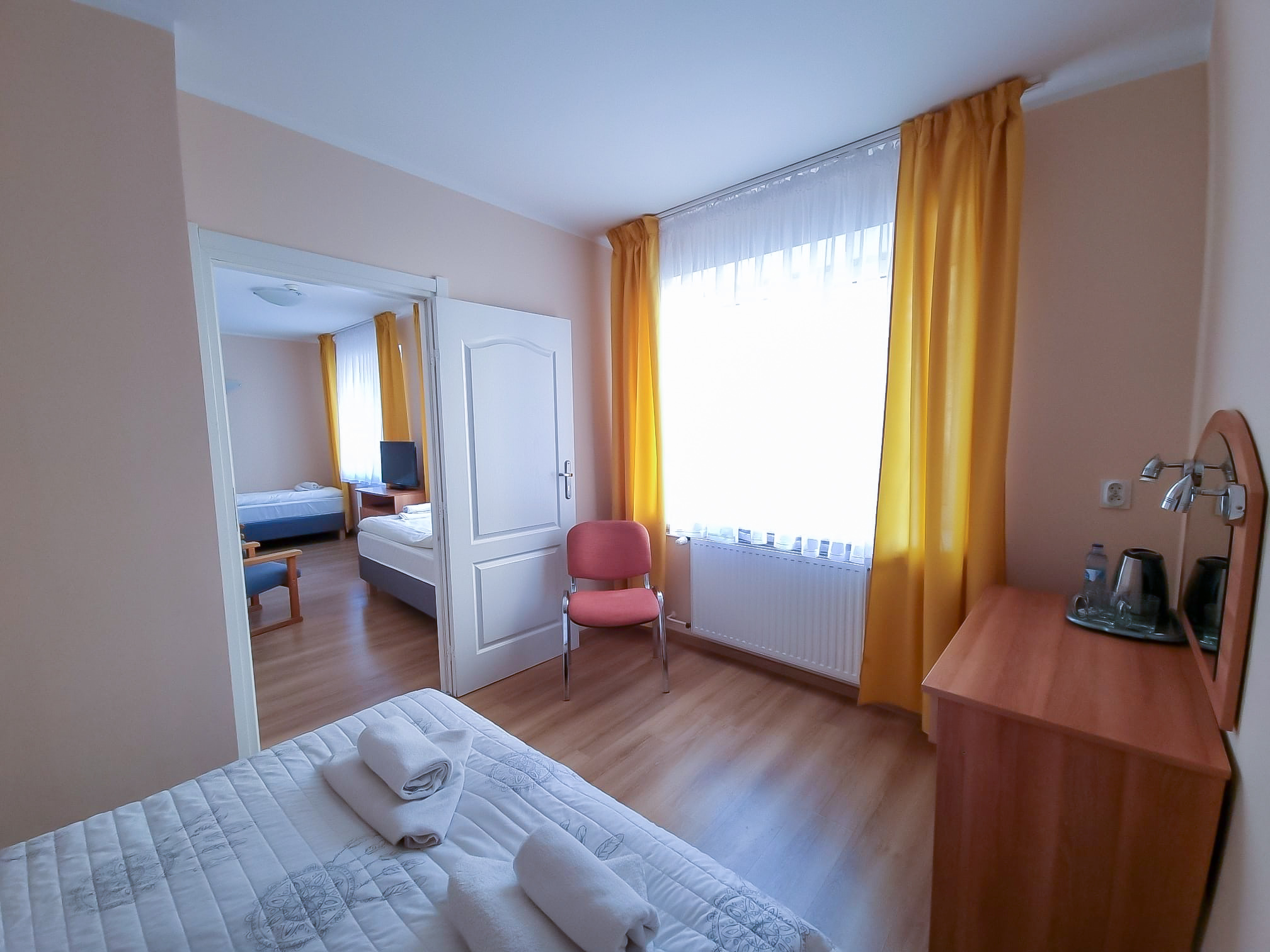 Jasny pokój hotelowy z łóżkiem, fotelem, biurkiem, telewizorem i żółtymi zasłonami