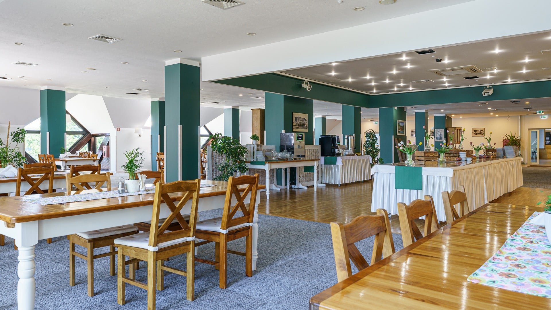 Jasna restauracja z drewnianymi stołami, krzesłami, bufetem i kwiatami na nakrytych stołach