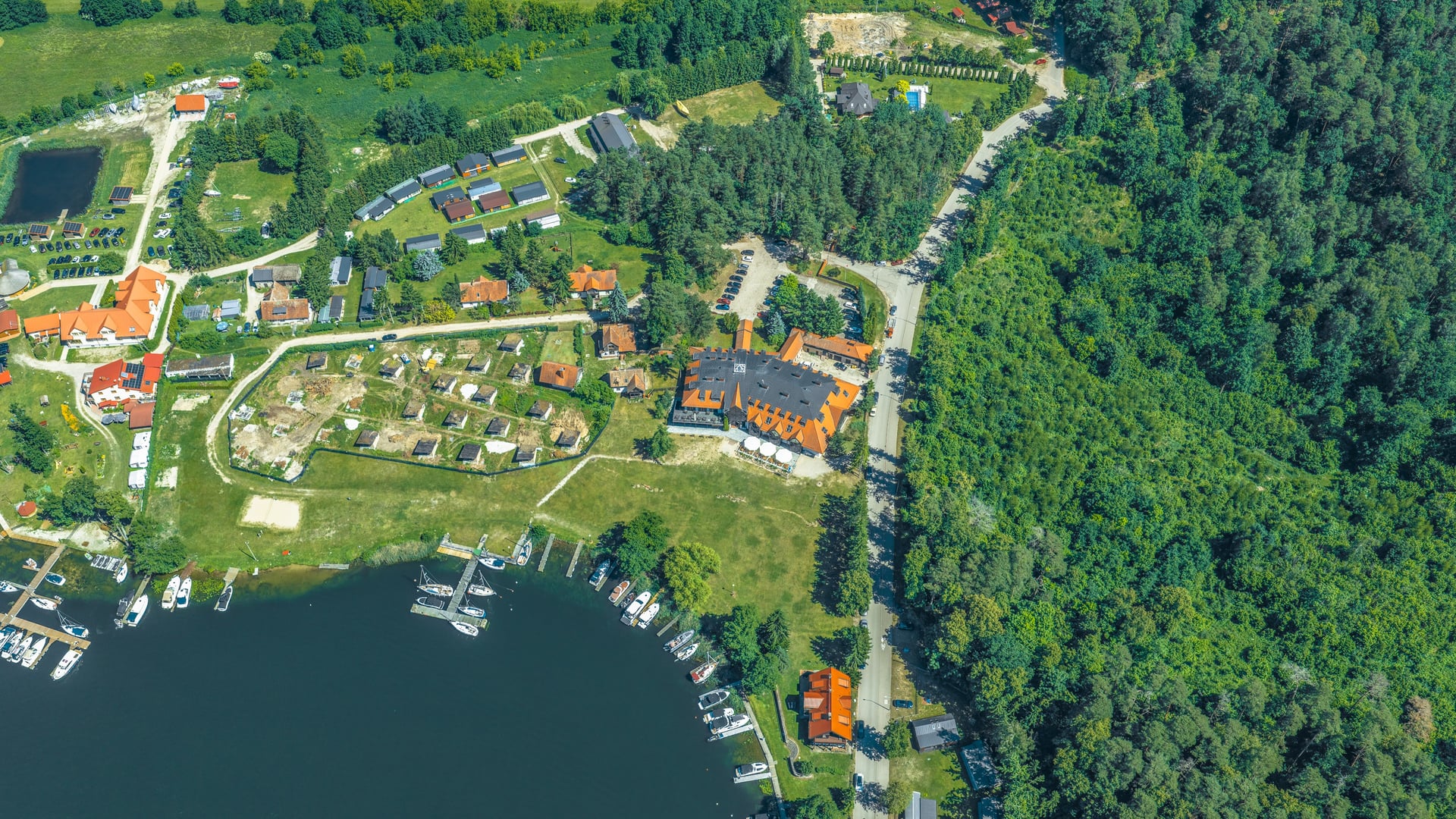 Widok z lotu ptaka na osadę nad jeziorem, przystań z łodziami, zabudowania i otaczający las